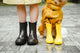 Dog in a yellow raincoat and boots beside its person