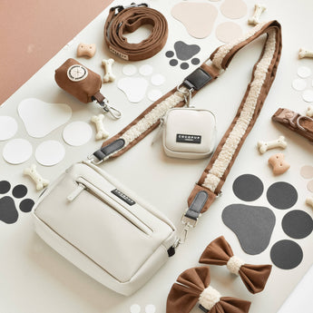 Brown Aviator strap attached to a cream dog-walking bag in a paw-print flat lay