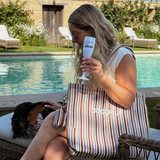 Woman seated by a pool with the Cocopup London striped tote bag and a dachshund