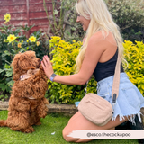 Woman kneeling in a garden beside a brown cockapoo while wearing Teddy Rupert bag