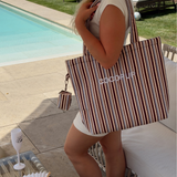 Woman carrying the brown and blue striped Cocopup London tote bag beside a pool