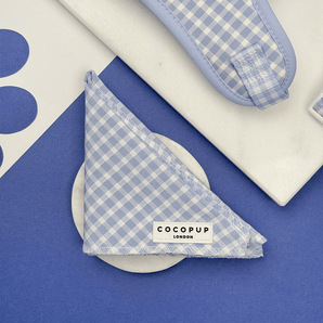 Cocopup London English Blue Bandana folded on a white dish in a blue flat lay