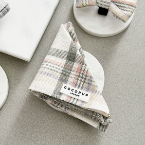 Cocopup London Oxford Plaid Bandana folded on a white dish in a neutral flat lay