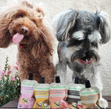 Two dogs behind a selection of Meaty Licks peanut butter pouches outdoors