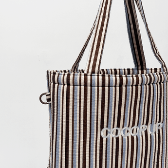 Close-up in studio van de hengsels en het geborduurde Cocopup London-logo op de gestreepte tas