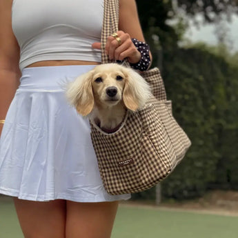 Woman carrying a small cream dog in the Cotswold Check carrier outdoors