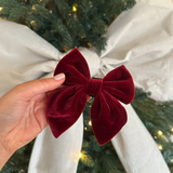 Hand holding the Cocopup London Berry Red Luxe Velvet Sailor Bow Tie in front of a cream festive ribbon