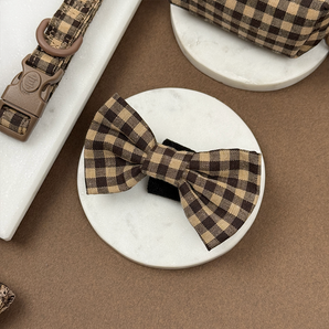 Cotswolds Check dog bow tie angled on a round stone tile beside matching accessories