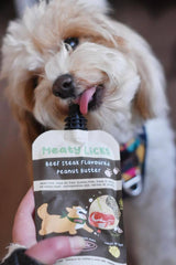 Small dog licking a Roast Beef Meaty Licks peanut butter pouch indoors