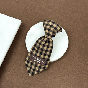 Cotswold Check dog tie angled on a round stone tile, showing brown check and brand label