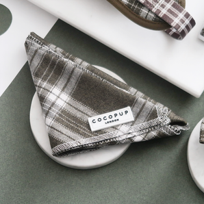Cocopup London Olive Check Bandana folded on a white dish in a green and neutral flat lay