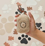 Hand met de crèmekleurige Teddy Rupert poepzakhouder, met zichtbare clip en ronde patch